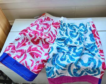 May include: A pair of white swim trunks with a pink and blue abstract pattern. The trunks have a blue trim at the top and a pink trim at the bottom.