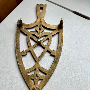 Pode incluir: Um descanso de panela de metal dourado com um design em forma de cora&ccedil;&atilde;o e quatro pernas. O descanso de panela &eacute; feito de um padr&atilde;o delicado e intrincado.