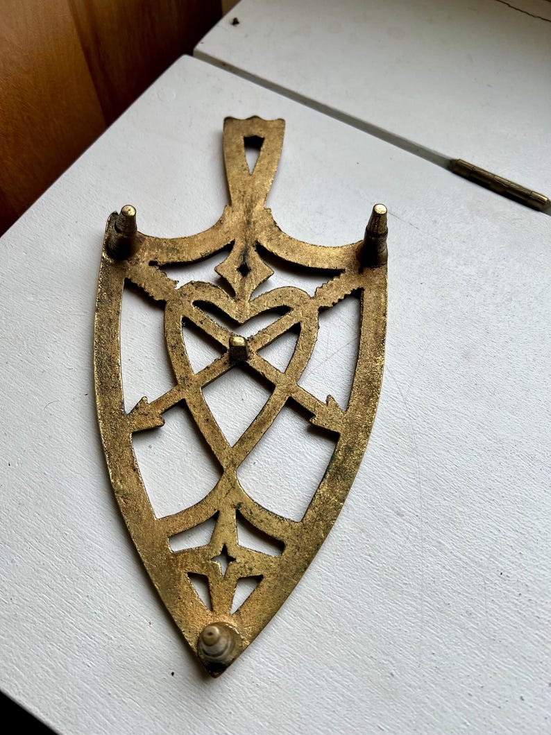 Pode incluir: Um descanso de panela de metal dourado com um design em forma de cora&ccedil;&atilde;o e quatro pernas. O descanso de panela &eacute; feito de um padr&atilde;o delicado e intrincado.