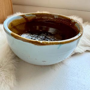 May include: A light blue ceramic bowl with a brown glaze and white speckles. The bowl is slightly chipped on the rim.