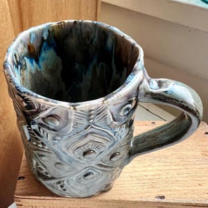 May include: A white ceramic mug with a black handle and the text "But First, Coffee" in a black, handwritten-style font. The mug is on a white surface.