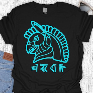May include: Black t-shirt featuring a turquoise graphic of a stylized bird head with a crown and symbols below. The design is a bold, single-color outline. The shirt is made of a soft material.