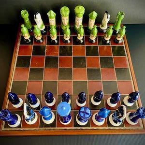 May include: A vintage chess set with green and blue ceramic pieces on a wooden board. The pieces are arranged in a starting position for a game of chess.