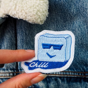Peut inclure: Un patch brodé bleu et blanc avec un glaçon souriant portant des lunettes de soleil et le mot "chill" en broderie bleue.