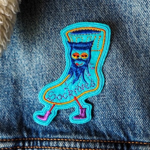 Pode incluir: Um remendo bordado azul e amarelo de uma meia com uma cara e a palavra "Socknotes" nele.