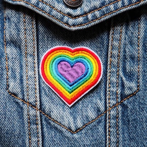 May include: A rainbow heart-shaped patch sewn onto a blue denim jacket.