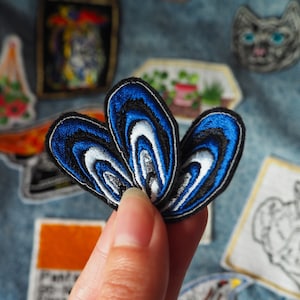 Op de afbeelding: Een blauwe en witte geborduurde patch met een waaiervormig ontwerp. De patch is gemaakt van stof en heeft een textuur.