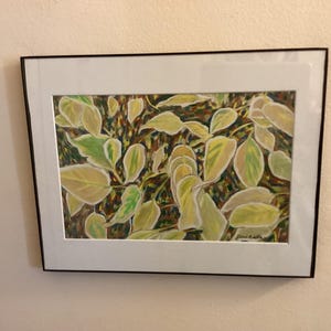 Peut inclure: Une œuvre encadrée représentant des feuilles détaillées dans des tons de jaune et de vert. Les feuilles sont posées sur un fond sombre. L'œuvre est encadrée d'un passe-partout blanc et d'un cadre noir.