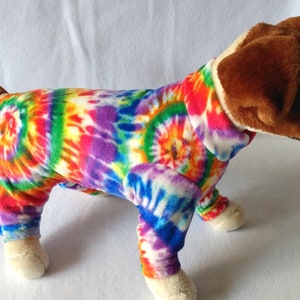 May include: A brown and white dog wearing a colorful tie-dye fleece pajamas. The pajamas have a rainbow swirl pattern.