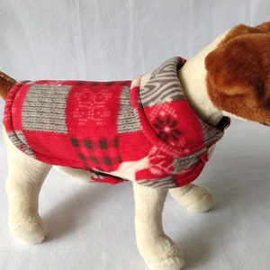 May include: Red and gray plaid dog sweater with a snowflake pattern. The sweater has a high neck and is made of fleece.
