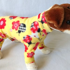 May include: A yellow dog pajamas with a ladybug and flower print. The pajamas are made of soft fleece and have a snug fit.