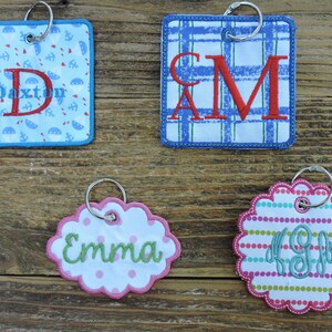 May include: Four personalized keychains with different designs and colors. The keychains feature the names "Dexton", "Cam", "Emma", and "Kgb" in embroidered lettering.