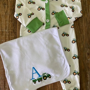 May include: White baby sleeper with green trim and a green tractor print.  The sleeper has a button closure.  A white burp cloth with green trim and a green tractor and the letter A embroidered in blue.