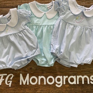 May include: Three baby girl's outfits with white collars and blue and white striped fabric. The outfits have a ruffled sleeve and are embroidered with a letter. The text "MFG Monograms" is visible at the bottom of the image.