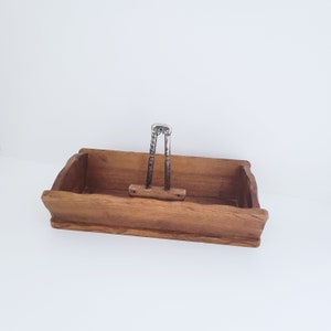 May include: A wooden nutcracker tray with a metal nutcracker inside. The tray is brown and has a rectangular shape. The nutcracker is silver and has a handle.