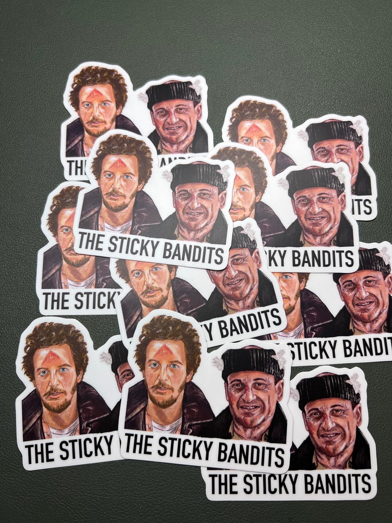以下が含まれることがあります： 「The Sticky Bandits」という文字が印刷された、男性のグループが描かれた白いステッカー12枚セット。男性は冬服を着ており、額に赤い点があります。