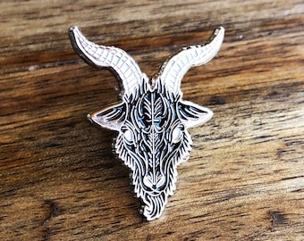 May include: A silver-toned enamel pin featuring a detailed black and white illustration of a goat's head with horns.