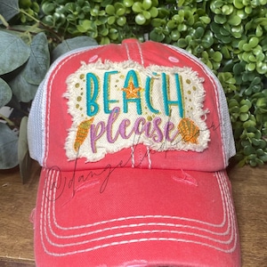 May include: Coral-colored distressed baseball cap with white mesh backing. The cap features the phrase "BEACH PLEASE" embroidered in turquoise and purple, with seashell and starfish accents. A stylish accessory for beach lovers.