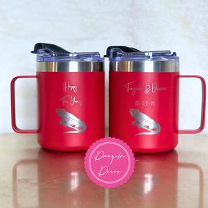 May include: Two red stainless steel mugs with handles and clear lids. The left mug features the text Happy Ten Years and an iguana graphic. The right mug features the text Tiara & Damon 12-23-14 and an iguana graphic. A pink circular logo reads Dangela Decor.