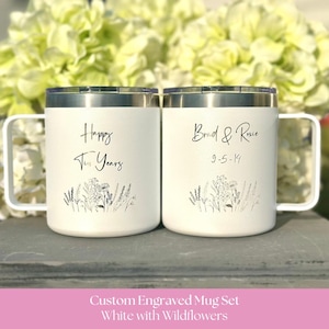 May include: Two white stainless steel mugs with handles and clear lids. The left mug features the text Happy Ten Years and a wildflower illustration. The right mug features the text Brad & Roxie 9-5-14 and a matching wildflower illustration.