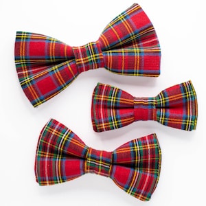 May include: Three red and green plaid bow ties of different sizes. The bow ties are arranged in a row from largest to smallest.