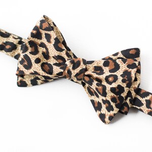 May include: A brown and black bow tie with a leopard print pattern.