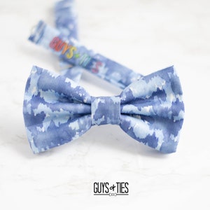 May include: A blue bow tie with a white watercolour cloud pattern. The bow tie is tied and ready to wear. The brand name "Guys + Ties" is printed below the bow tie.