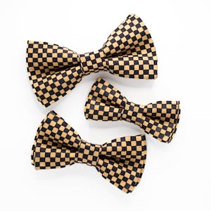 May include: Three checkered bow ties in different sizes. The bow ties are black and gold with a checkered pattern.
