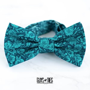 Pode incluir: Gravata borboleta azul turquesa com padrão floral. A gravata borboleta tem um fundo azul escuro com um padrão floral azul turquesa claro.
