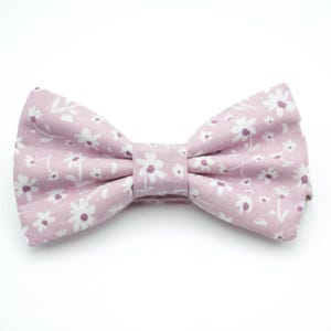 May include: A pink bow tie with a white floral pattern.