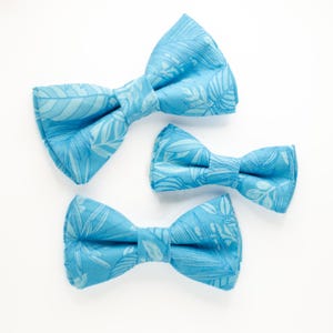 May include: Three blue bow ties with a white leaf pattern. The bow ties are arranged in a size order from largest to smallest.
