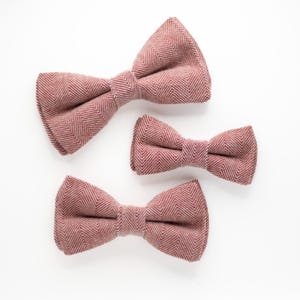May include: Three bow ties in different sizes, all made of a pink and white herringbone patterned fabric.