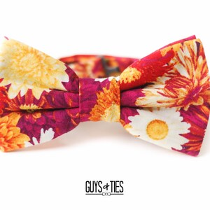 May include: A floral bow tie with a red, orange, and yellow pattern. The bow tie is made of fabric and has a self-tie closure.