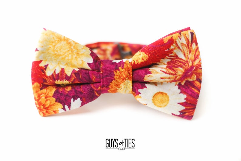 May include: A floral bow tie with a red, orange, and yellow pattern. The bow tie is made of fabric and has a self-tie closure.