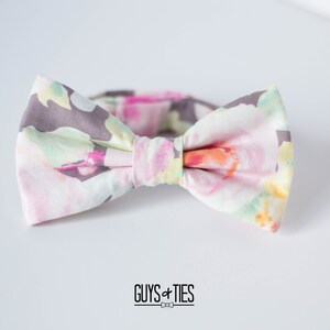 May include: A bow tie with a floral pattern in shades of pink, green, yellow, and gray. The bow tie is tied and ready to wear.