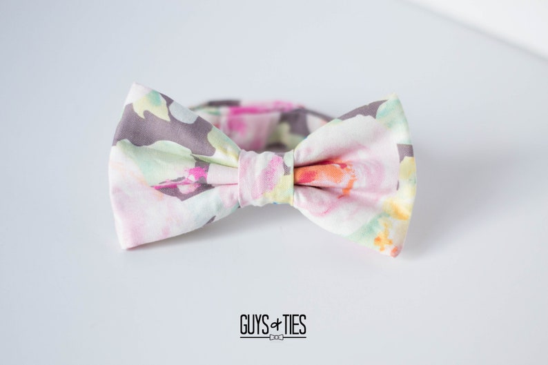 May include: A bow tie with a floral pattern in shades of pink, green, yellow, and gray. The bow tie is tied and ready to wear.