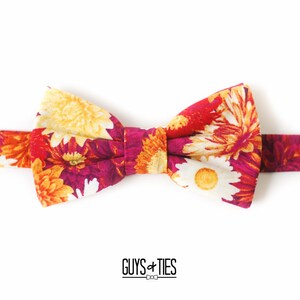 May include: A floral bow tie with a red, orange, and yellow pattern. The bow tie is made of fabric and has a white background.