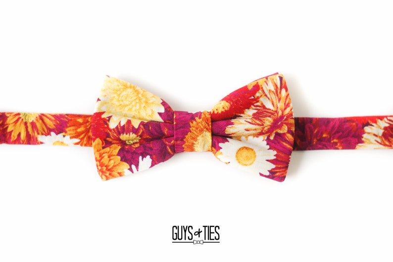 May include: A floral bow tie with a red, orange, and yellow pattern. The bow tie is made of fabric and has a white background.