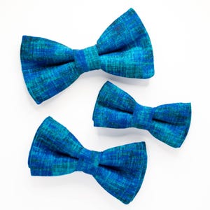 May include: Three blue bow ties with a green and blue plaid pattern. The bow ties are arranged in a size order from largest to smallest.