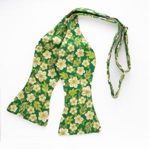 May include: A green bow tie with a white floral pattern. The bow tie has a long strap for adjusting the fit.