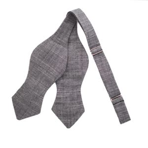 May include: A gray bow tie with a textured fabric and adjustable strap. The bow tie is made of a linen blend and has a pointed shape.