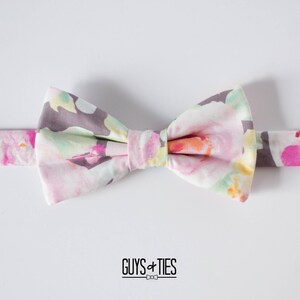 May include: A floral patterned bow tie with a gray background and pink, yellow, and green flowers. The bow tie is tied and ready to wear.