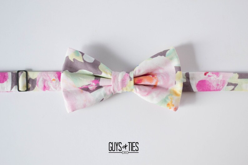 May include: A floral patterned bow tie with a gray background and pink, yellow, and green flowers. The bow tie is tied and ready to wear.