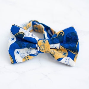 Puede incluir: Una pajarita azul y amarilla con un patrón de mandos de videojuegos.