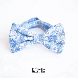 May include: A blue bow tie with a white floral pattern. The bow tie is made of cotton fabric and has a classic design.