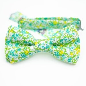 May include: A green and white bow tie with a floral pattern. The bow tie is made of fabric and has a light green background with white and yellow flowers.