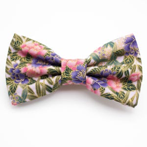 May include: A bow tie with a floral pattern in shades of pink, purple, and green on a white background.