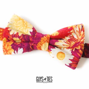 May include: A floral bow tie with a red, white, and yellow pattern. The bow tie is made of fabric and has a classic bow shape.