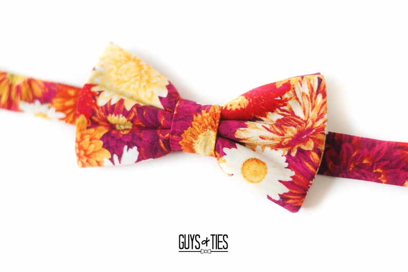 May include: A floral bow tie with a red, white, and yellow pattern. The bow tie is made of fabric and has a classic bow shape.