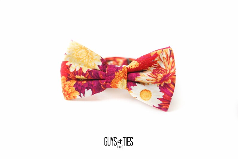 May include: A floral bow tie with a red, orange, yellow, and white pattern. The bow tie is made of fabric and has a classic bow shape.